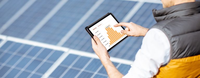 Man examining genaration of solar power plant, holding digital tablet with a chart of electricity production. Concept of online monitoring of the electric station
